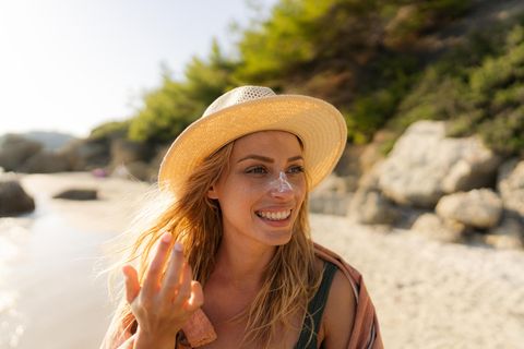 Frau cremt sich am Strand mit Sonnencreme ein