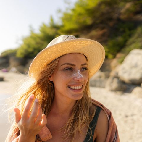 Frau cremt sich am Strand mit Sonnencreme ein