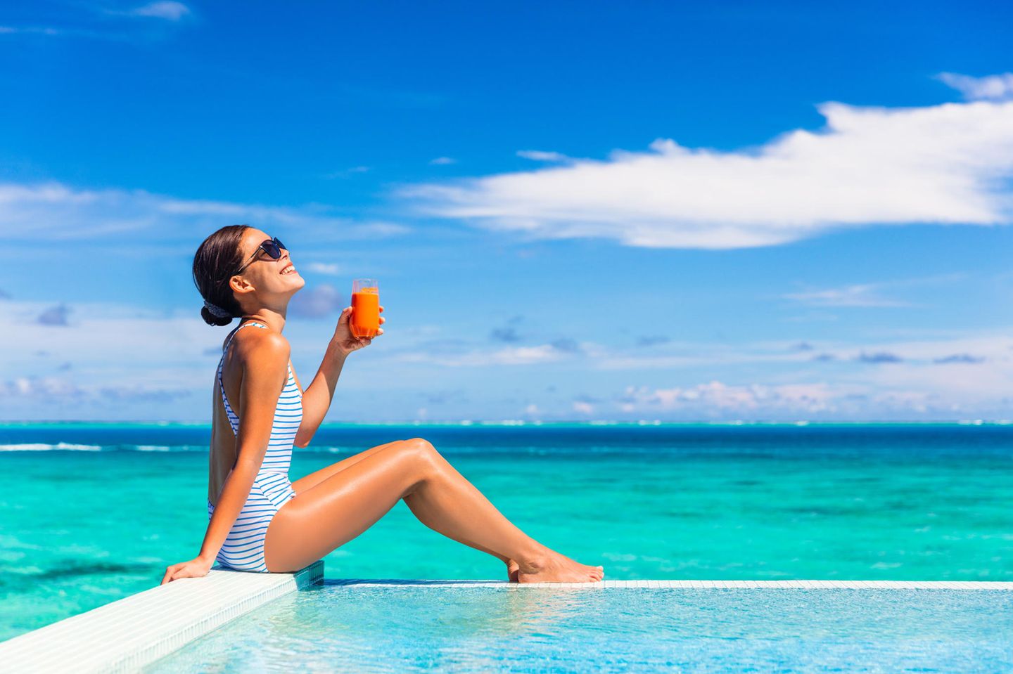 Ein Frau sonnt sich am Strand und hält ein Glas Möhrensaft in der Hand