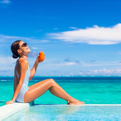 Ein Frau sonnt sich am Strand und hält ein Glas Möhrensaft in der Hand