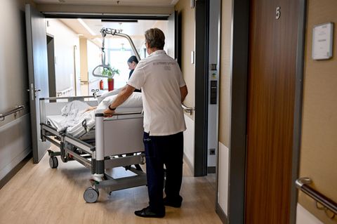 Zur Krankenhausreform: In einem Krankenhaus schieben ein Mann und eine Frau ein Bett mit einer Patientin darin über einen Flur