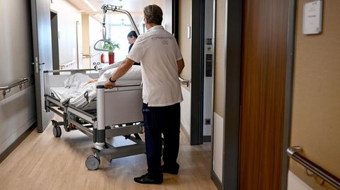 Zur Krankenhausreform: In einem Krankenhaus schieben ein Mann und eine Frau ein Bett mit einer Patientin darin über einen Flur
