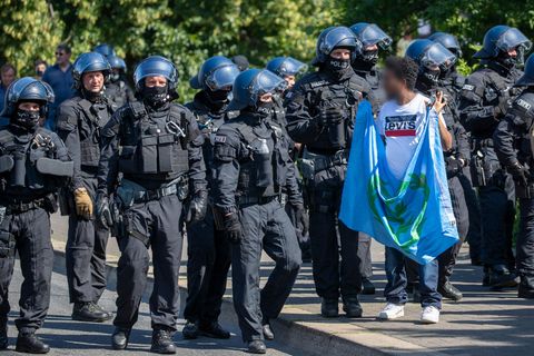 Ein Mann mit einer Flagge in den erhobenen Händen wendet sich einer Polizei-Kette zu