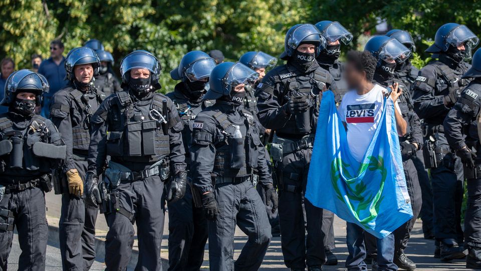 Ein Mann mit einer Flagge in den erhobenen Händen wendet sich einer Polizei-Kette zu