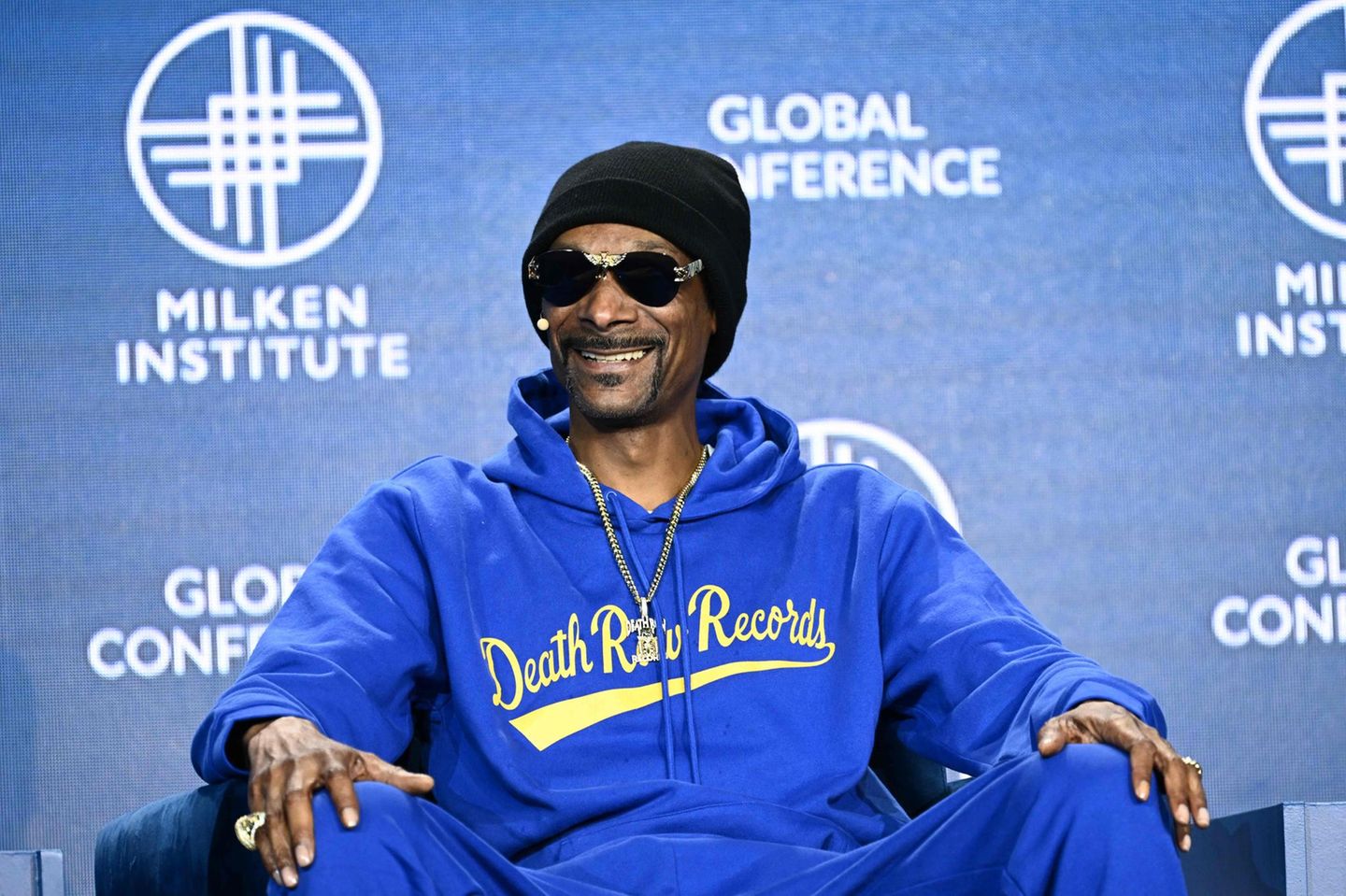 Im Cannabis-Geschäft: Rapper Snoop Dogg sitzt mit einer Mütze und Sonnenbrille lächelnd auf einem Sofa