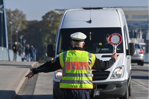 Ein Polizist mit Warnweste und Kelle winkt einen weißen Transporter für eine Kontrolle aus dem Verkehr in Brandenburg