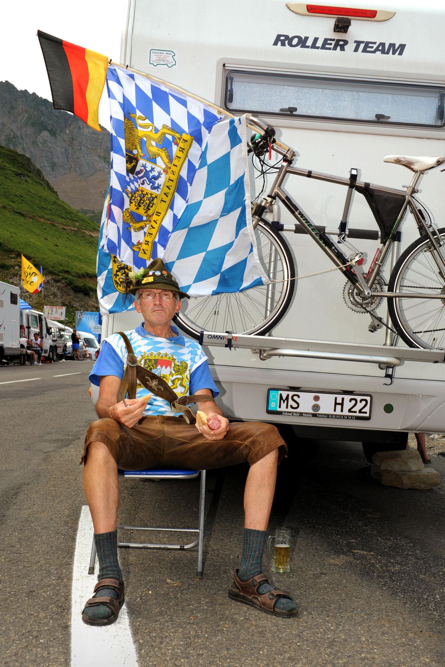 Ein Mann mit Lederhose, Wurst und Stulle am Rande der Tour de France