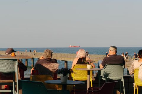 Menschen sitzen mit Blick aufs Meer und ein Tankschiff an der Promenade