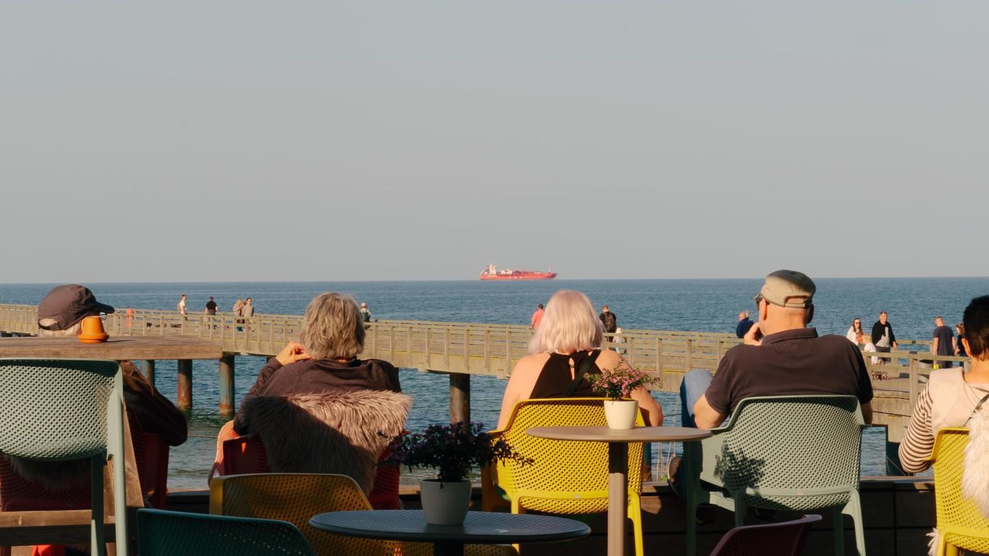 Menschen sitzen mit Blick aufs Meer und ein Tankschiff an der Promenade Menschen sitzen mit Blick aufs Meer und ein Tankschiff an der Promenade
