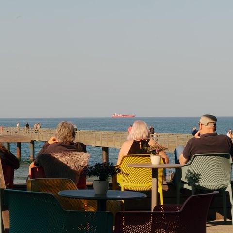 Menschen sitzen mit Blick aufs Meer und ein Tankschiff an der Promenade