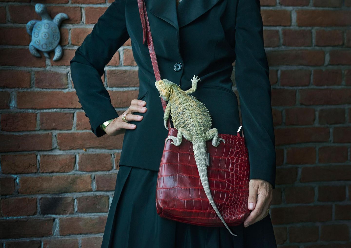 Auf der roten Handtasche einer Frau sitzt eine grüne Echse