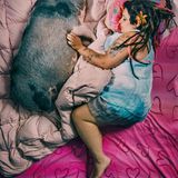 Eine Mutter im Kleid liegt in ihrem Bett, neben sich ihr Hausschwein