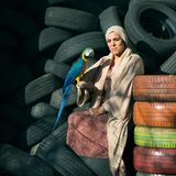 Eine Frau sitzt auf einem Reifenstapel und hält ihren Papagei auf dem Arm