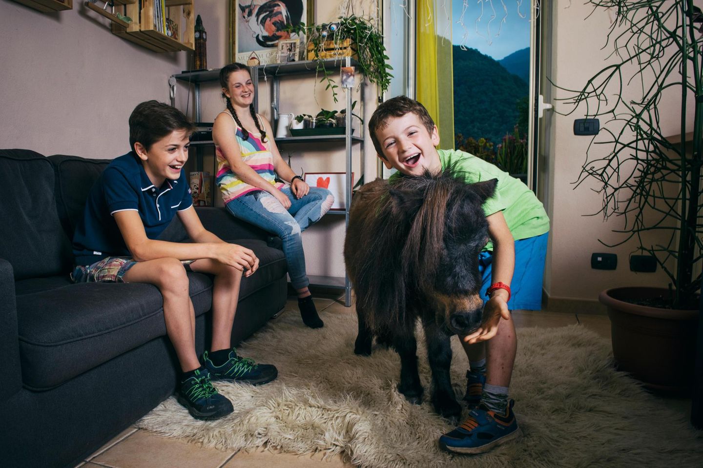 Drei Geschwister freuen sich in ihrem Wohnzimmer über ihr Pony