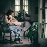 Eine Frau sitzt in einem Schaukelstuhl und umarmt eine Gans auf ihrem Schoß