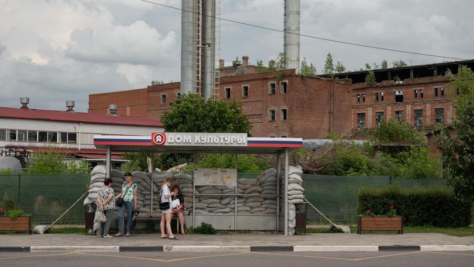 Menschen stehen an einer Bushaltestelle in Russland, die mit Sandsäcken umgeben ist