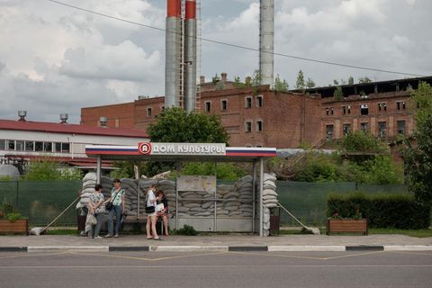 Menschen stehen an einer Bushaltestelle in Russland, die mit Sandsäcken umgeben ist