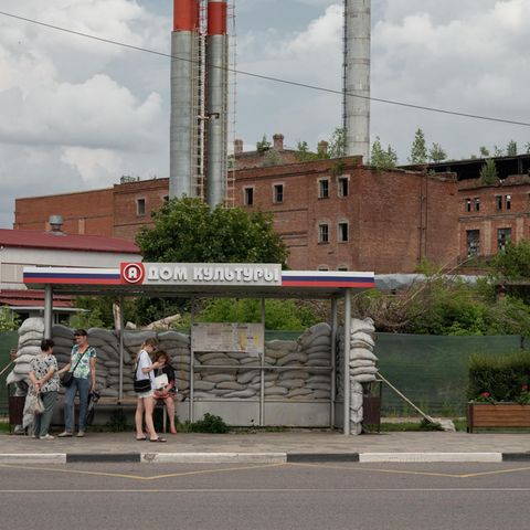 Menschen stehen an einer Bushaltestelle in Russland, die mit Sandsäcken umgeben ist