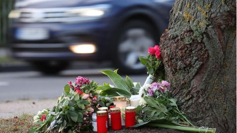 Blumen, Kerzen und Grablichter stehen am Straßenrand an einem Baum