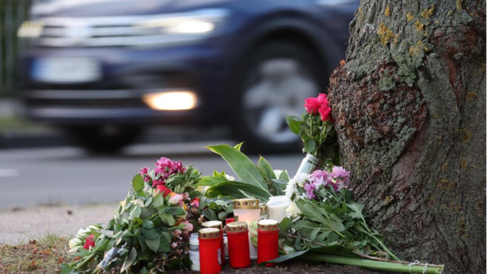 Blumen, Kerzen und Grablichter stehen am Straßenrand an einem Baum