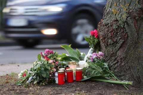 Blumen, Kerzen und Grablichter stehen am Straßenrand an einem Baum