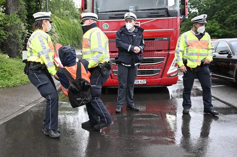Polizisten tragen einen Klimaaktivisten von einer Straße, wo er einen roten LKW blockiert hatte