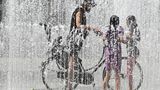 Ein Radfahrer fährt bei den heißen Temperaturen durch einen Springbrunnen um sich abzukühlen. Im unterfränkischen Kitzingen wurde mit 38,0 Grad die bisher höchste Temperatur in diesem Jahr gemessen.