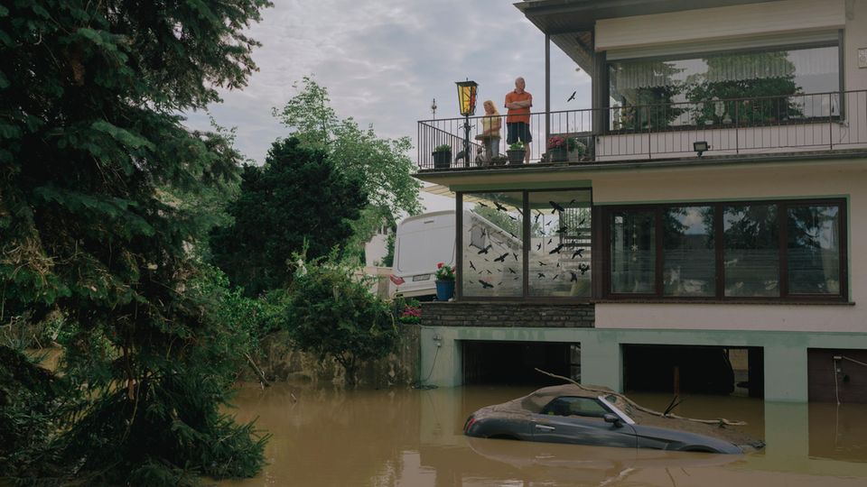 Ein Paar steht auf dem Balkon eines Hauses, das Wasser auf der Straße reicht bis zum ersten Stock