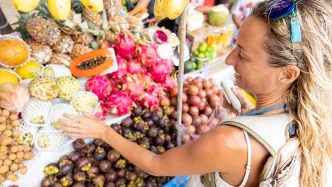 Frau wählt bei eienr Fernreise an einem Straßenstrand Obst aus