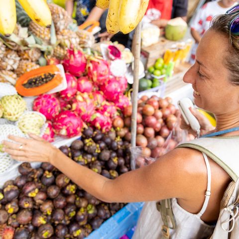 Frau wählt bei eienr Fernreise an einem Straßenstrand Obst aus