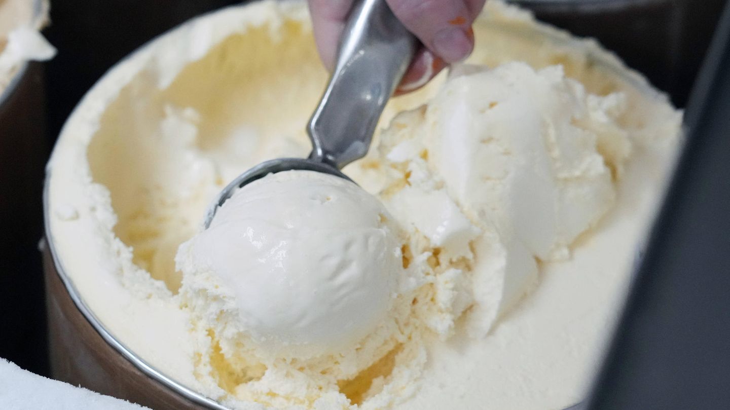 Eine Hand portioniert eine Kugel Vanille-Eis