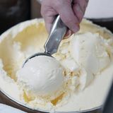 Eine Hand portioniert eine Kugel Vanille-Eis