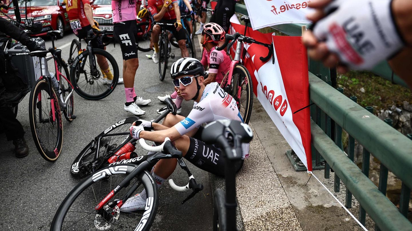 Tour-Favorit Tadej Pogacar vom Team UAE macht es sich auf dem Randstein der Brücke bequem. Er nimmt die Unterbrechung sichtlich gelassen, wie es seine Art ist.