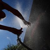 Im bayerischen Kaufbeuren kühlt sich eine Frau in einem Garten mit Wasser aus einem Gartenschlauch ab