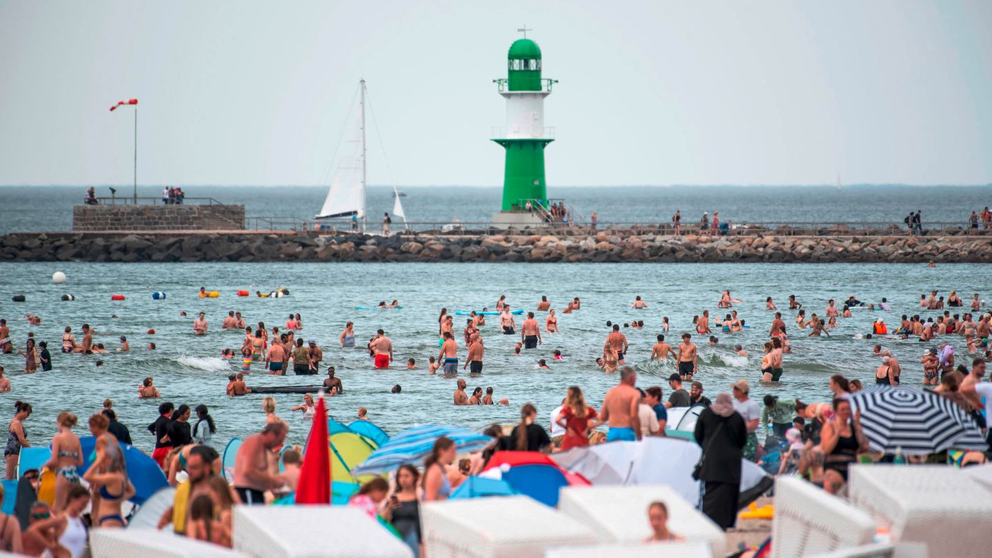 Badegäste am Stand von Warnemünde, im Hintergrund ist der Leuchtturm zu sehen