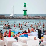Badegäste am Stand von Warnemünde, im Hintergrund ist der Leuchtturm zu sehen