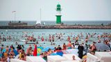 Badegäste am Stand von Warnemünde, im Hintergrund ist der Leuchtturm zu sehen