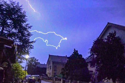 Ein Blitz ist am dunkelblauen Himmel über Häusern zu sehen