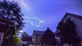 Ein Blitz ist am dunkelblauen Himmel über Häusern zu sehen