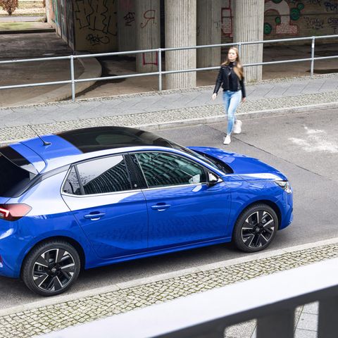 Ein Auto steht vor einem Parkhaus. Eine Frau geht darauf zu