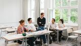 Fünf Schüler:innen sitzen zusammen beim Lernen in einem Klassenzimmer