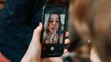 Junge Frau fährt sich mit Handykamera als Spiegel die Lippen nach