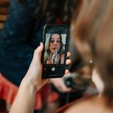 Junge Frau fährt sich mit Handykamera als Spiegel die Lippen nach