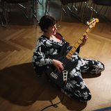 Junge Frau kniet mit Bass auf dem Boden und spielt