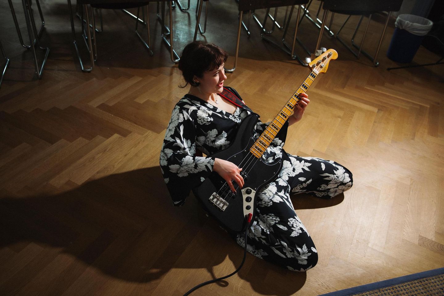 Junge Frau kniet mit Bass auf dem Boden und spielt