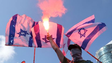 Ein Protestant hält einen Bengalo in die Luft vor israelischen Flaggen