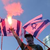 Ein Protestant hält einen Bengalo in die Luft vor israelischen Flaggen