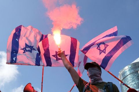 Ein Protestant hält einen Bengalo in die Luft vor israelischen Flaggen