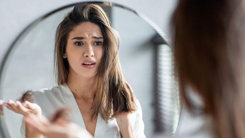 Eine Frau schaut sich im Spiegel ihr dünnes Haar an.
