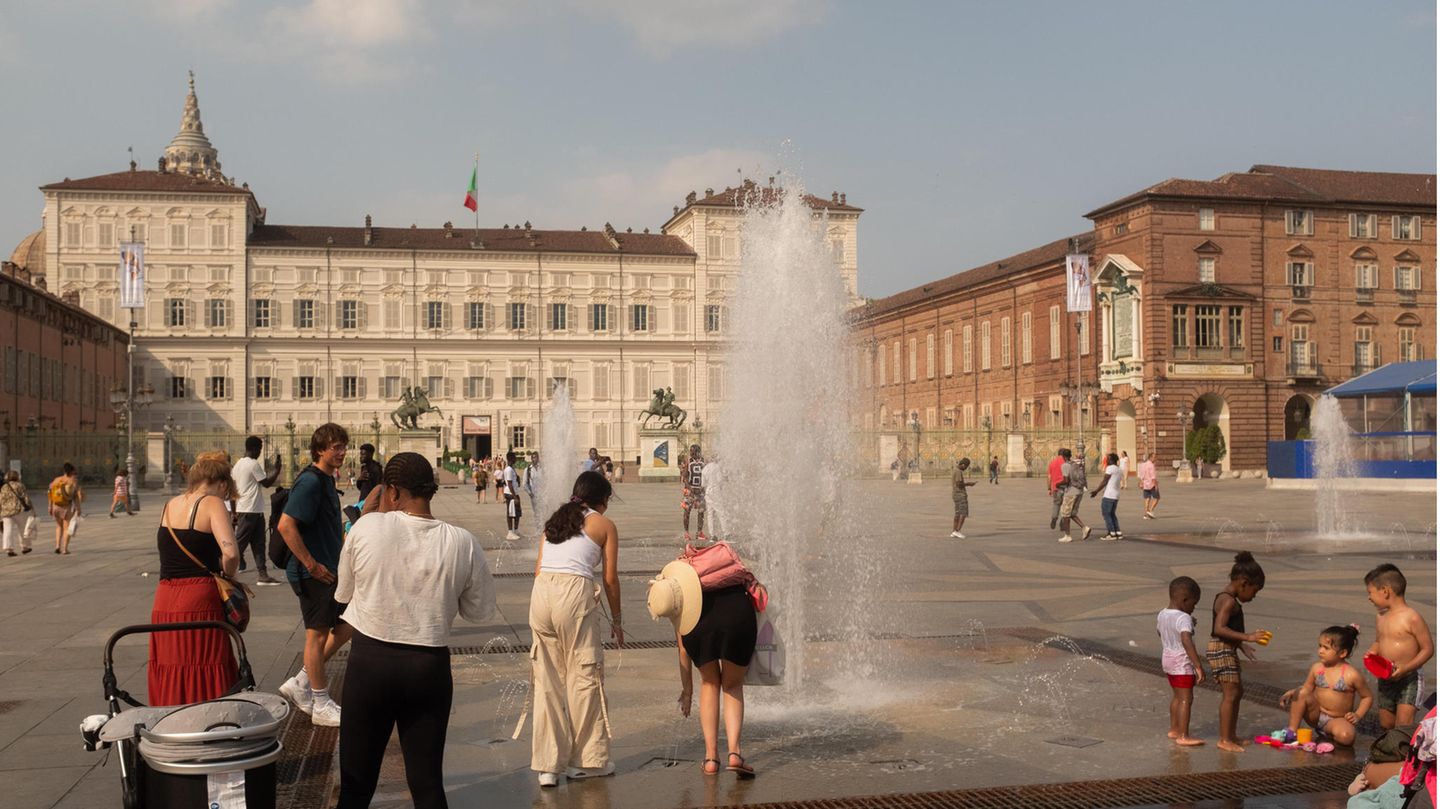 Auf einem Platz vor einem Stadtschloss in Turin stehen Menschen an einer kleinen Fontäne